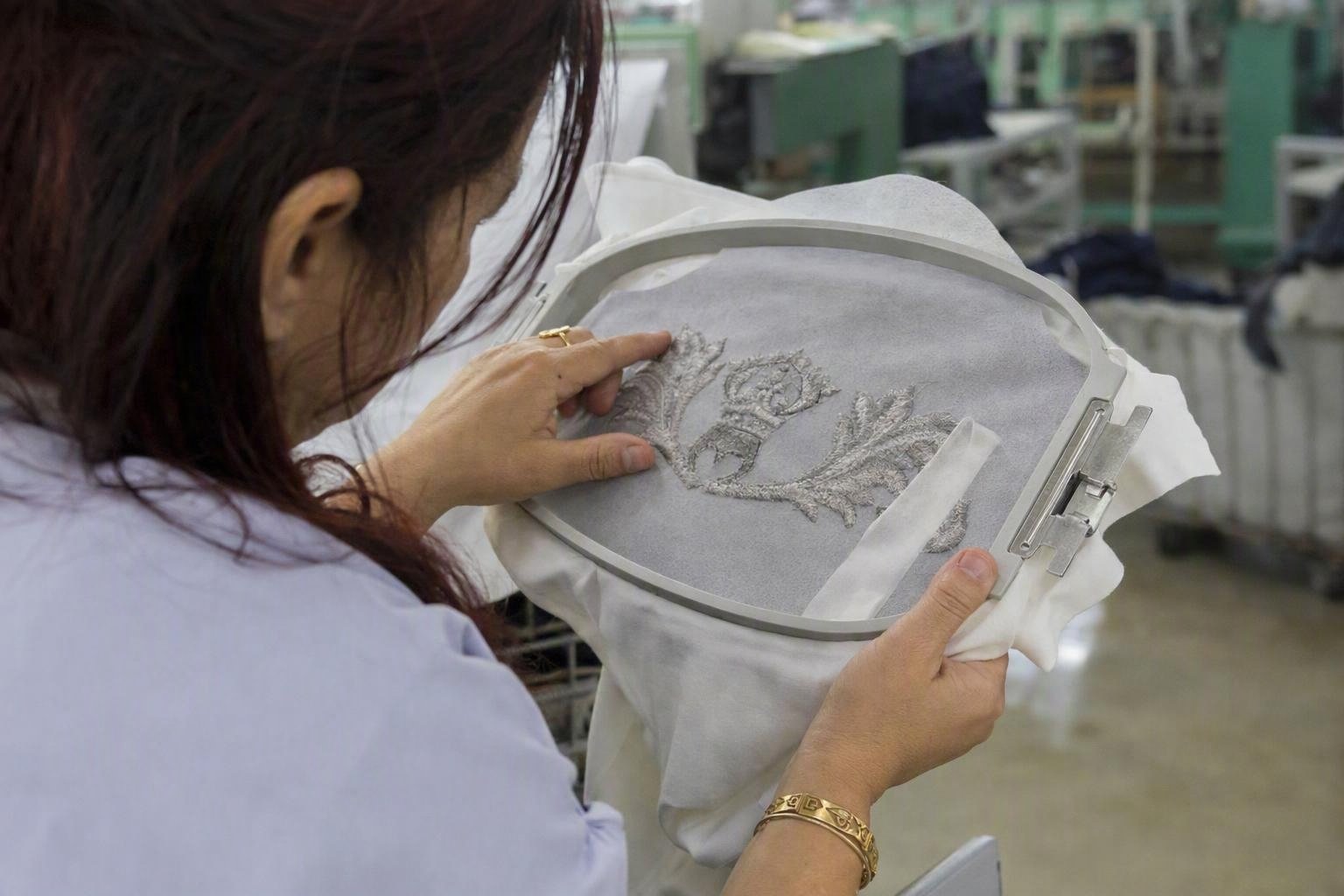 Contrôle d’une broderie sur maille encore cerclée, avec stabilisateur visible au revers et vérification des contours, de la densité et du tirage.