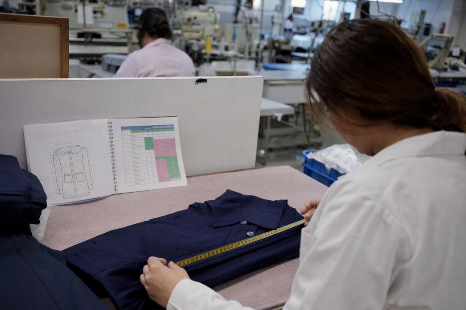 Une contrôleuse compare les mesures d’un uniforme scolaire fini au patron de référence et au tableau de tolérances.